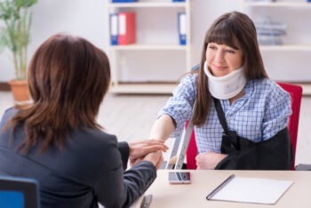 A woman with a neck brace and arm sling is shaking hands with her lawyer.